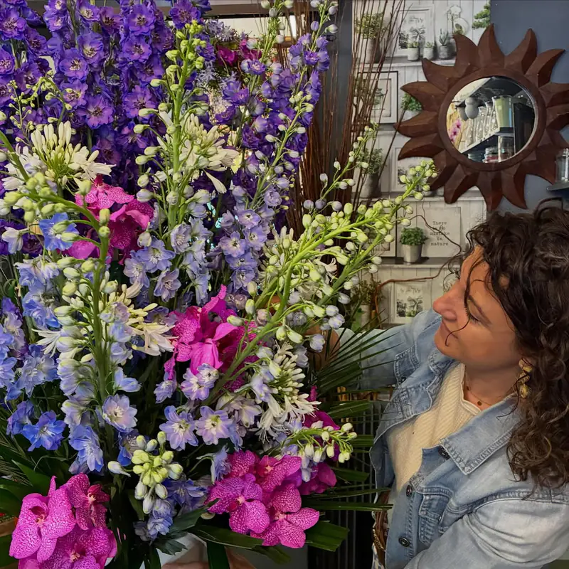 Fleuriste composant un grand bouquet de delphiniums, orchidées et lisianthus